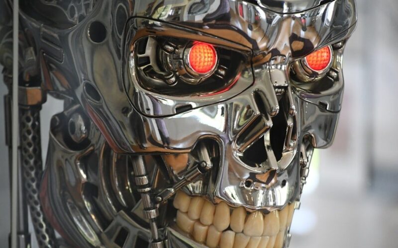Chrome humanoid robot skull with glowing red eyes and exposed teeth