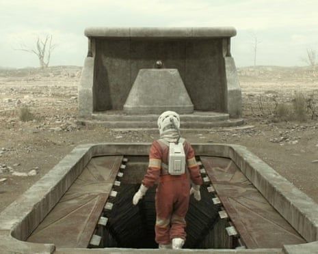 Person in a red suit entering a concrete underground bunker in a barren landscape